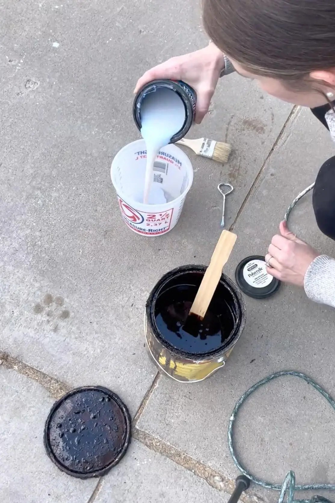 A DIYer pours polycrylic into a measuring cup, preparing a protective finish for wooden shelves.